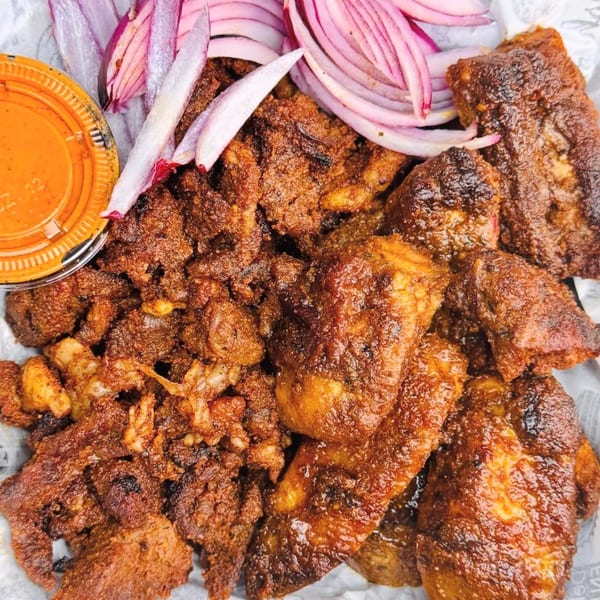 Close-up of crispy fried meat pieces with red onion slices and a side of orange sauce.