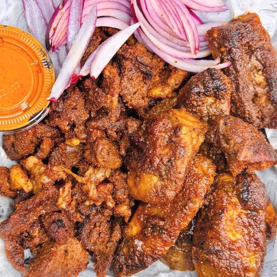 Close-up of crispy fried meat pieces with red onion slices and a side of orange sauce.