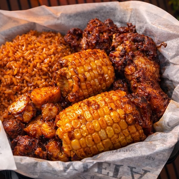 Close-up of a basket with spicy chicken wings, corn on the cob, and rice.