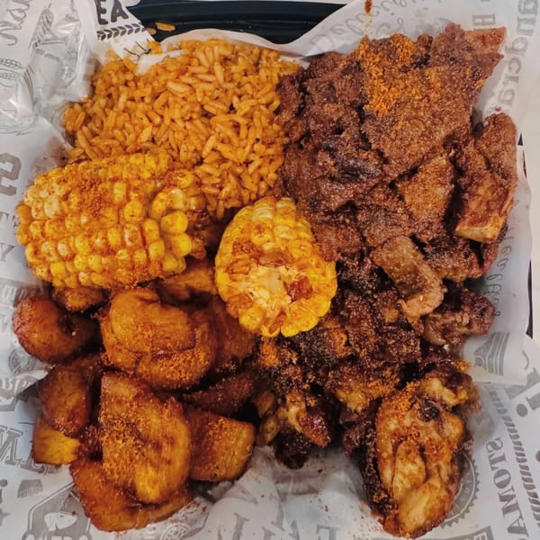 A platter of seasoned rice, corn on the cob, fried plantains, and grilled meat.