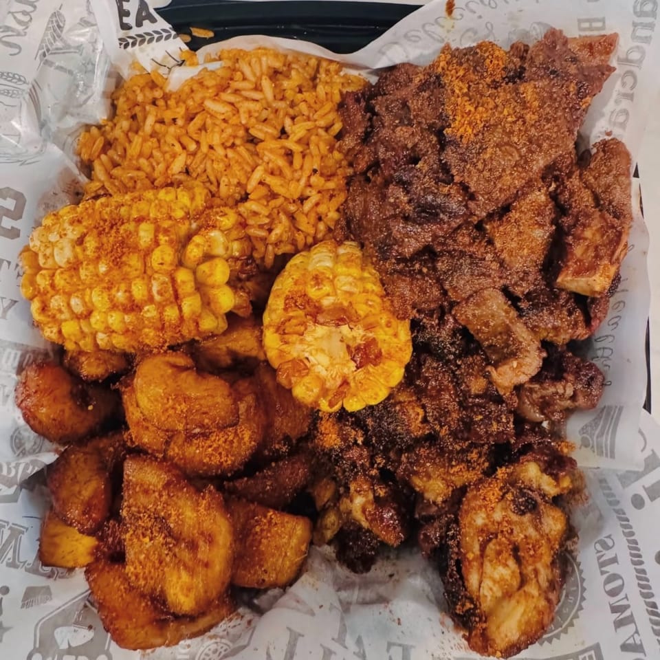 A platter of seasoned rice, corn on the cob, fried plantains, and grilled meat.